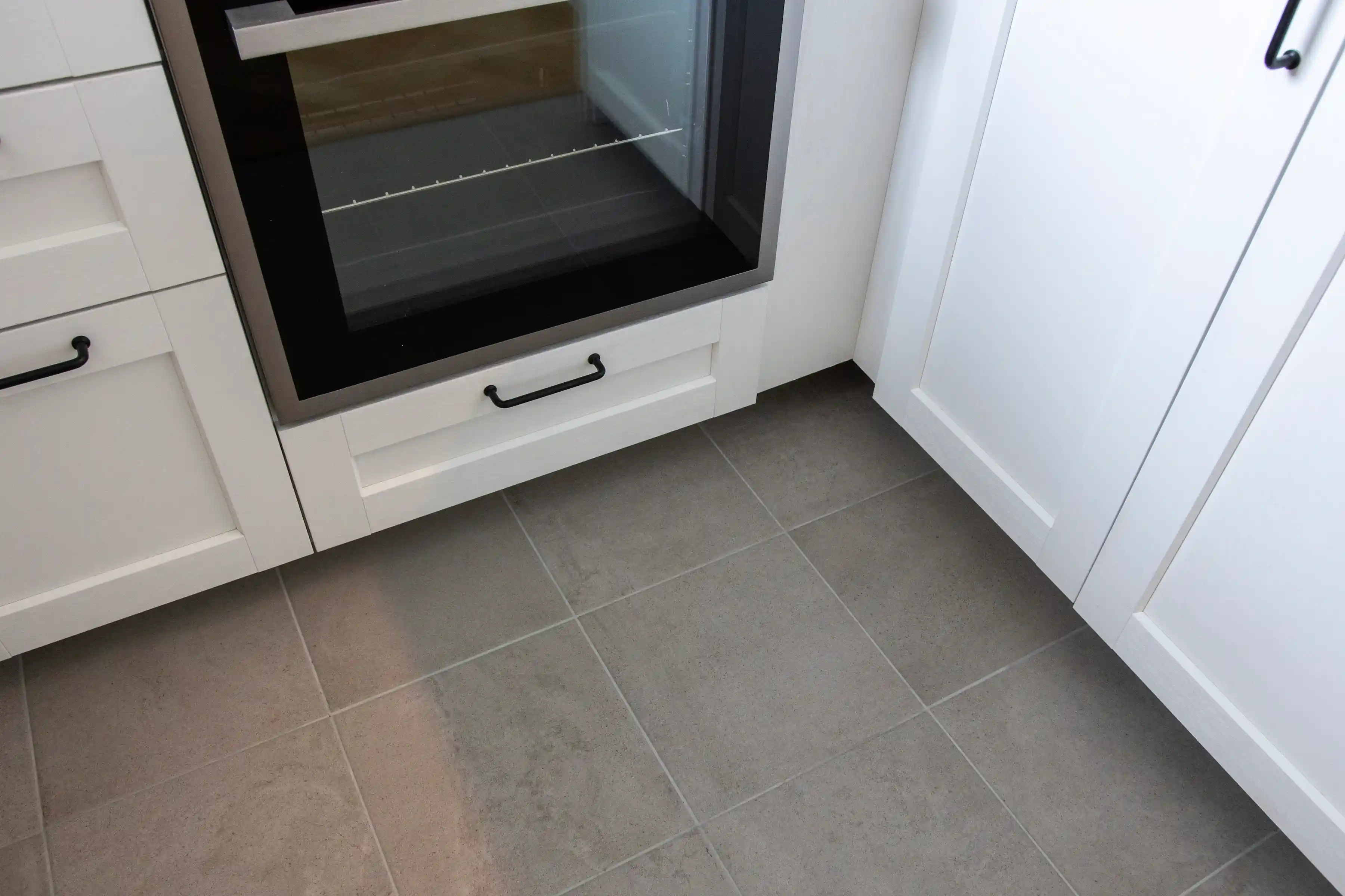 Gråa golvplattor och vita köksluckor