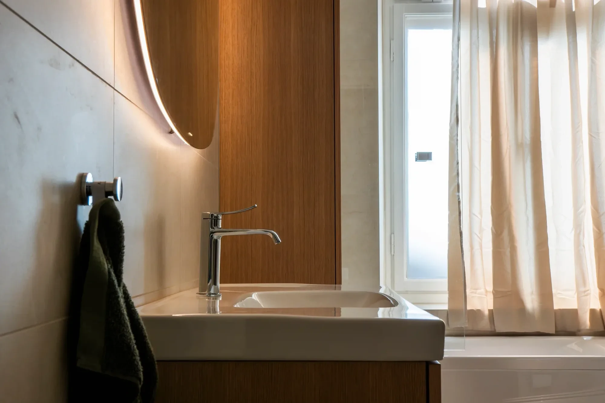 Renoverat badrum i Stockholm med handfat, träpanel och rund spegel med belysning